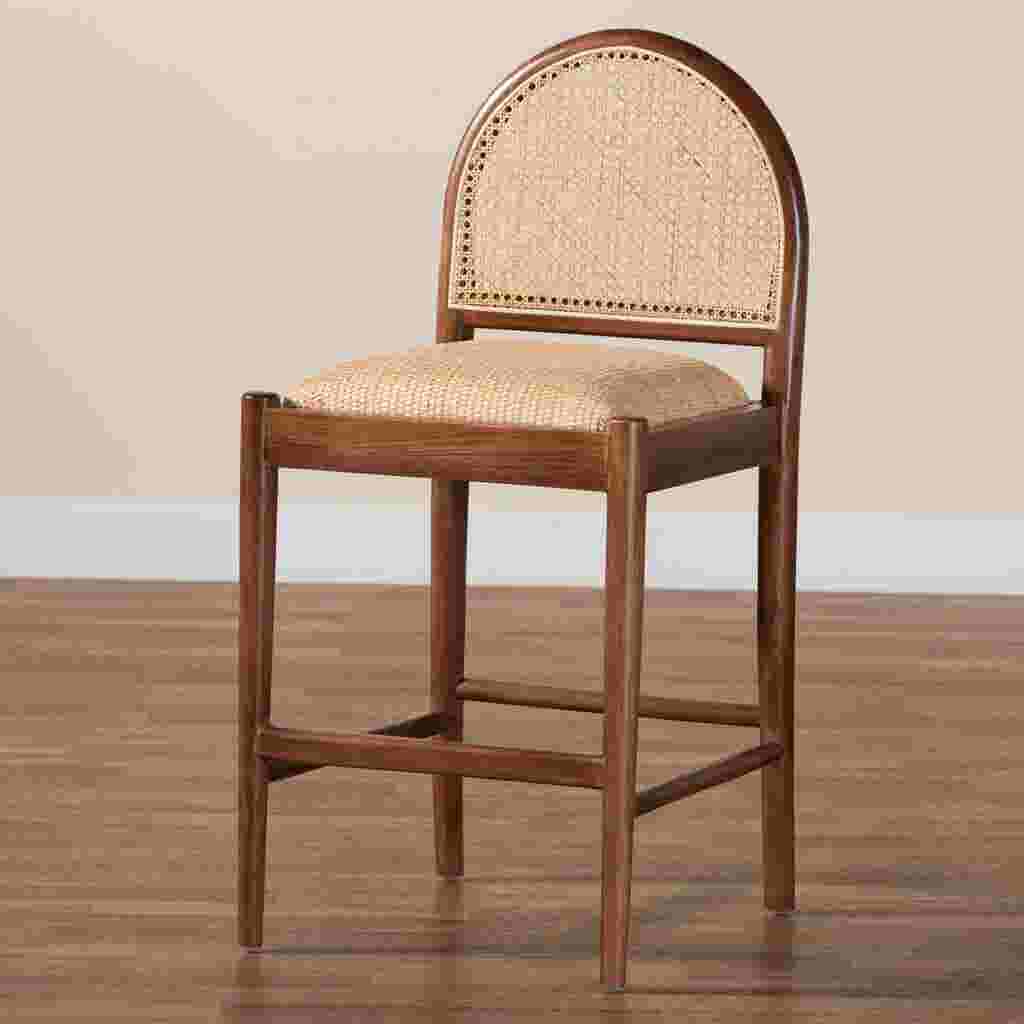 A wooden counter stool with a woven cane back and seat, placed on a wooden floor against a plain wall.