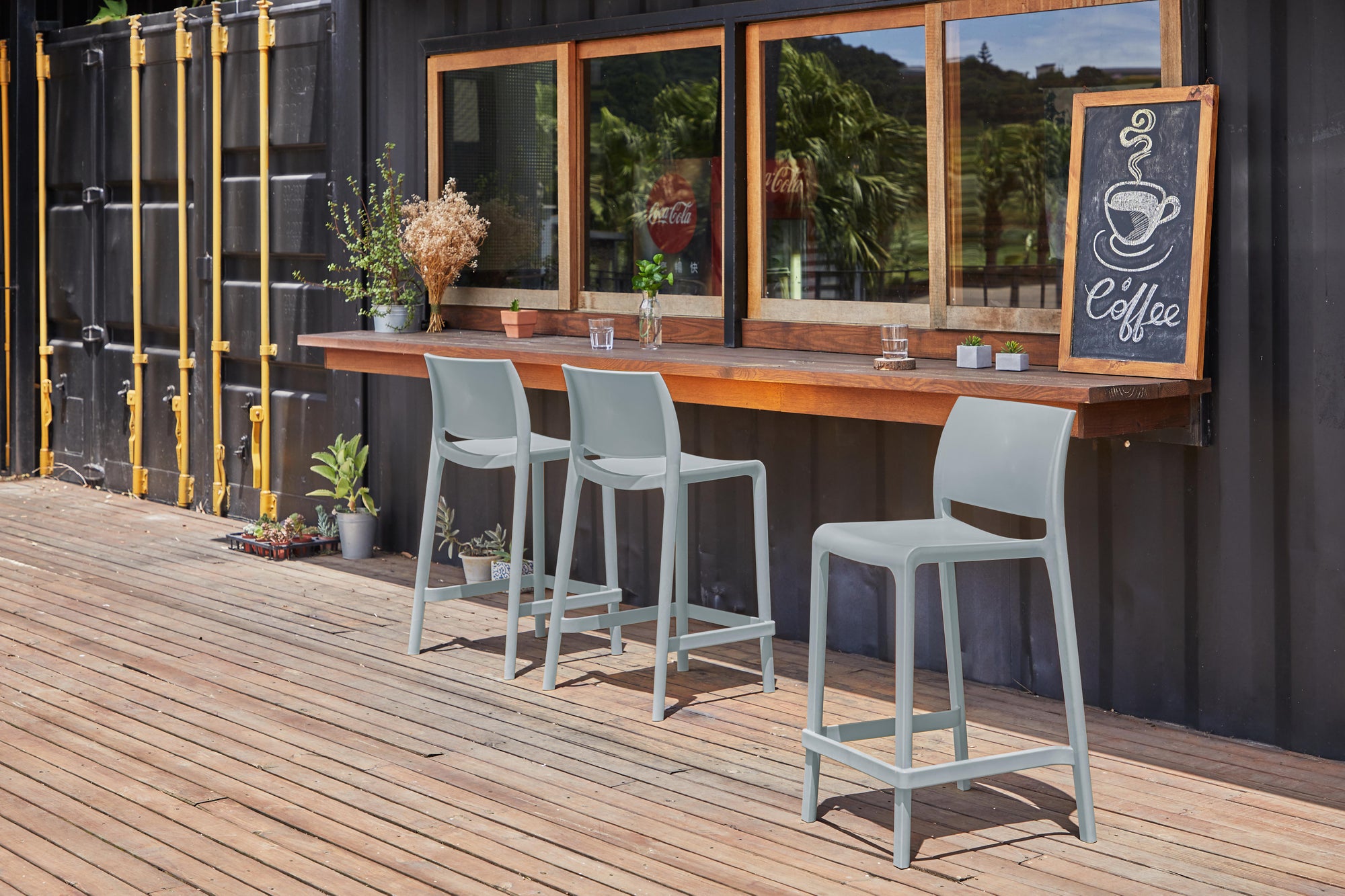 Two light sage outdoor counter stools arranged on a wooden deck.